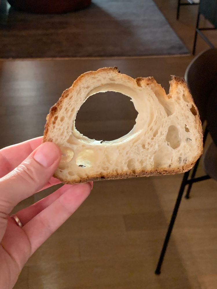 A slice of sourdough bread which has a significant hole in it from an air bubble during baking
