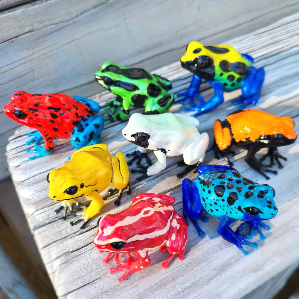 a bunch of dart frog figures of various species, all different on a wooden chair arm 