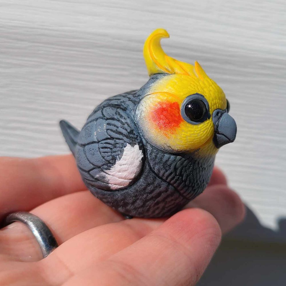 a sculpture of a cockatiel in someone's hand that is more round than a real cockatiel 
