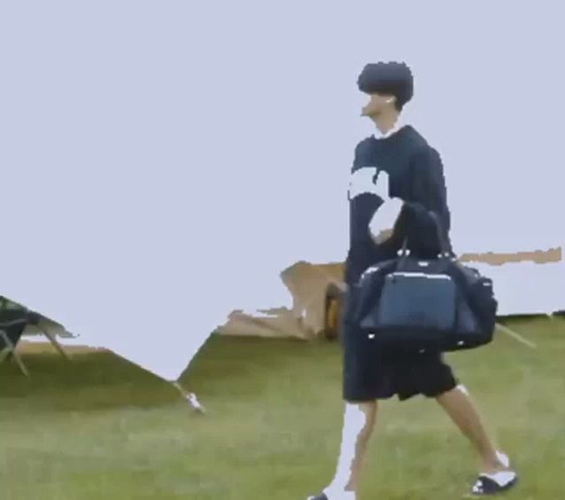 a man is standing in the grass holding a bag