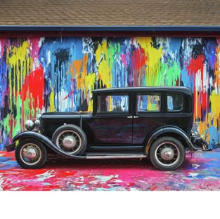 A Model T Ford, painted black, in front of a wall coloured in paint splashes