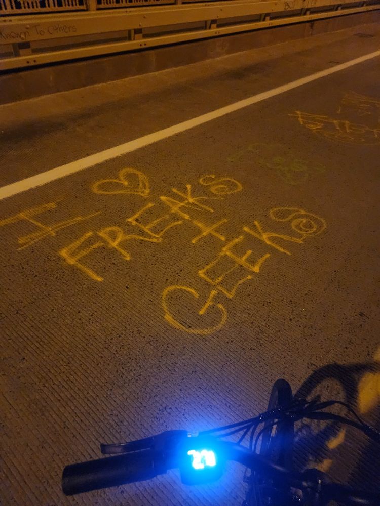 Graffitti on a road, spraypainted "I <3 FREAKS + GEEKS"