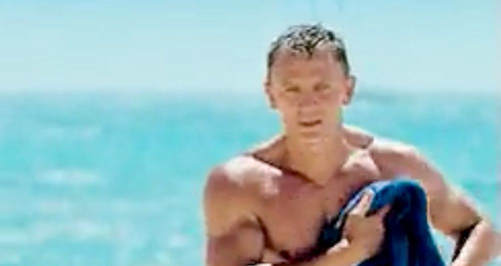 Screenshot of a GIF of Daniel Craig walking into foreground with the background being water.
The viewer just sees his shirtless upper body as he dries himself with a towel.