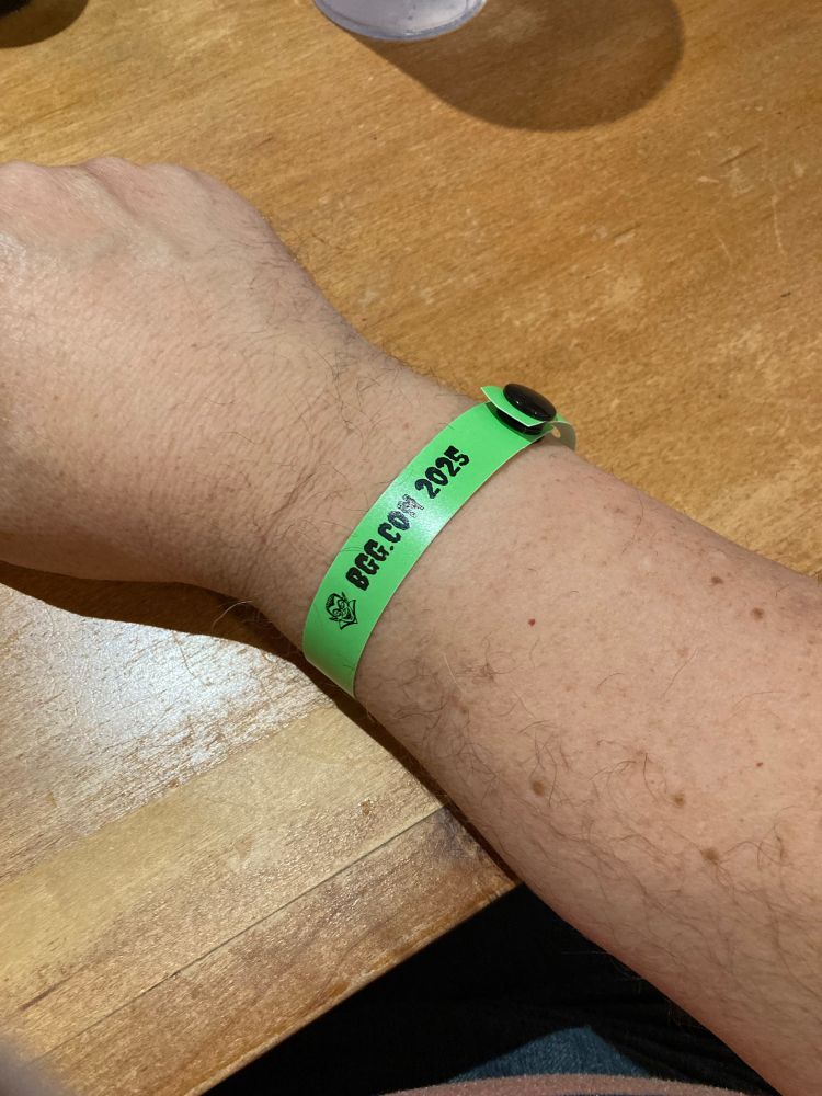 An arm still wearing a bright green wristband. It says BGG Con 2025.