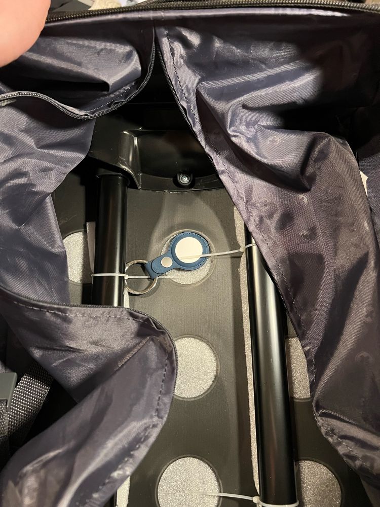 The inside of a carryon suitcase. The liner has been zipped open to reveal an airtag hidden underneath it.