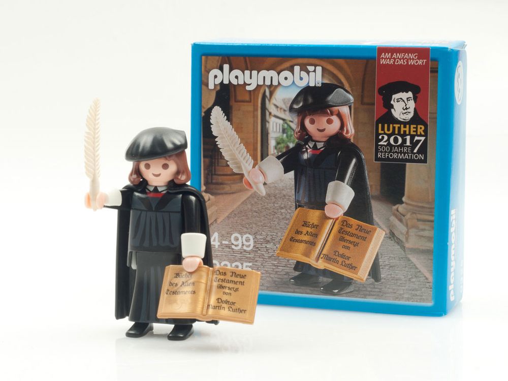 A Playmobil figure of Martin Luther holding a quill and a bible.