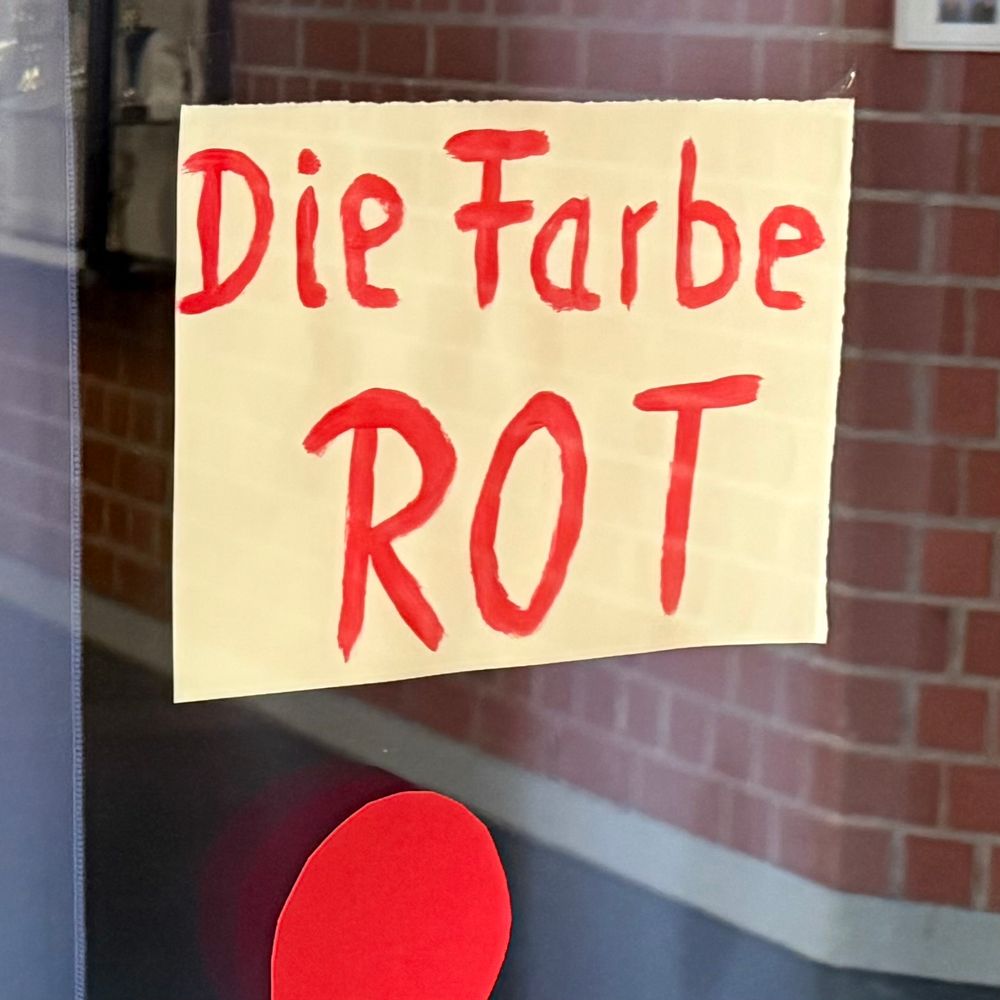 Handgeschriebenes Plakat „Die Farbe ROT“ mit einem roten Punkt unterhalb des Plakats