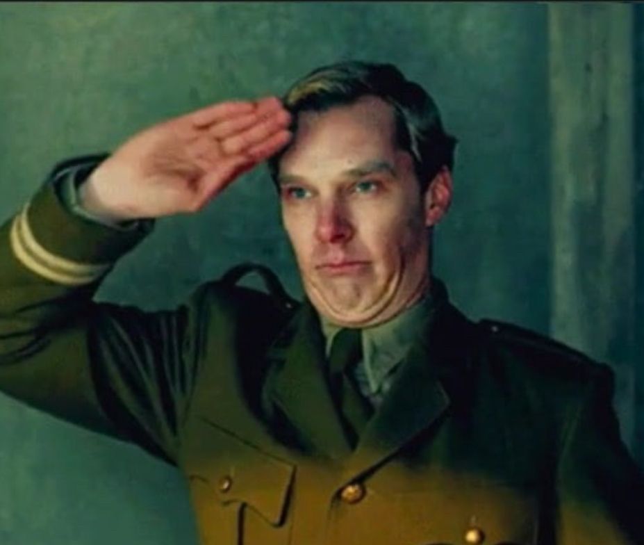 Beneficiary Cumberbun, in a green military suit uniform, saluting with his palm facing out. He looks quite sickly.
