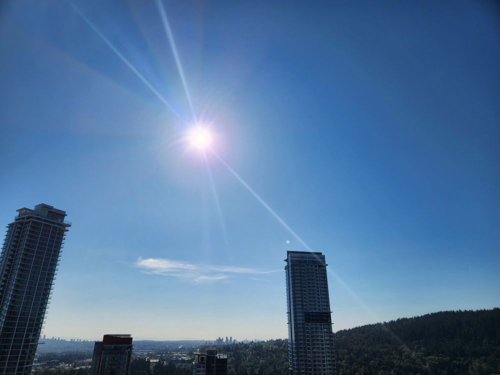 Blue sky with the sun shining brightly. There's a lems flare making it look like rays are shooting out of the sun. 