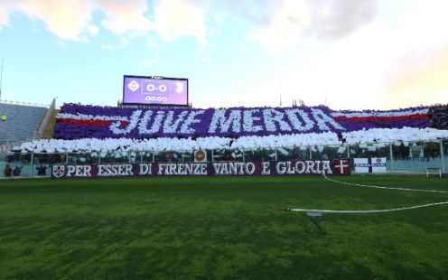 A football field , some stands and a violet and white choreography with juve mer*a written by viola ultras curva fiesole
