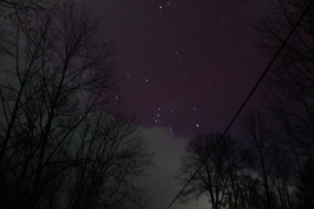 the constellation orion lit by red auroral glow, partially obscured by green-tinged clouds
