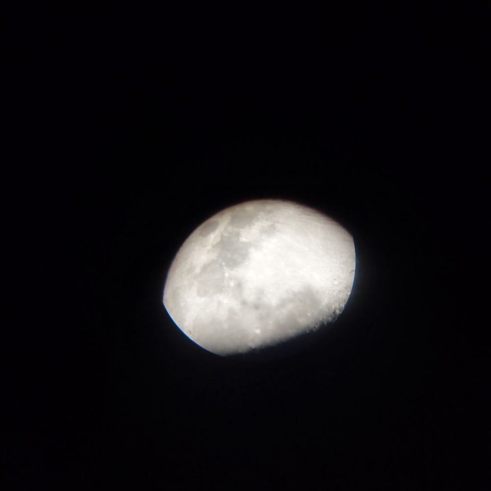 Photo of a waxing gibbons moon, partially occluded by the side of the 9mm eyepiece of the telescope that the picture was taken through.