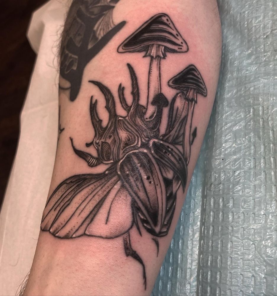 A tattoo on a wrist of a beetle with mushrooms growing out of its body