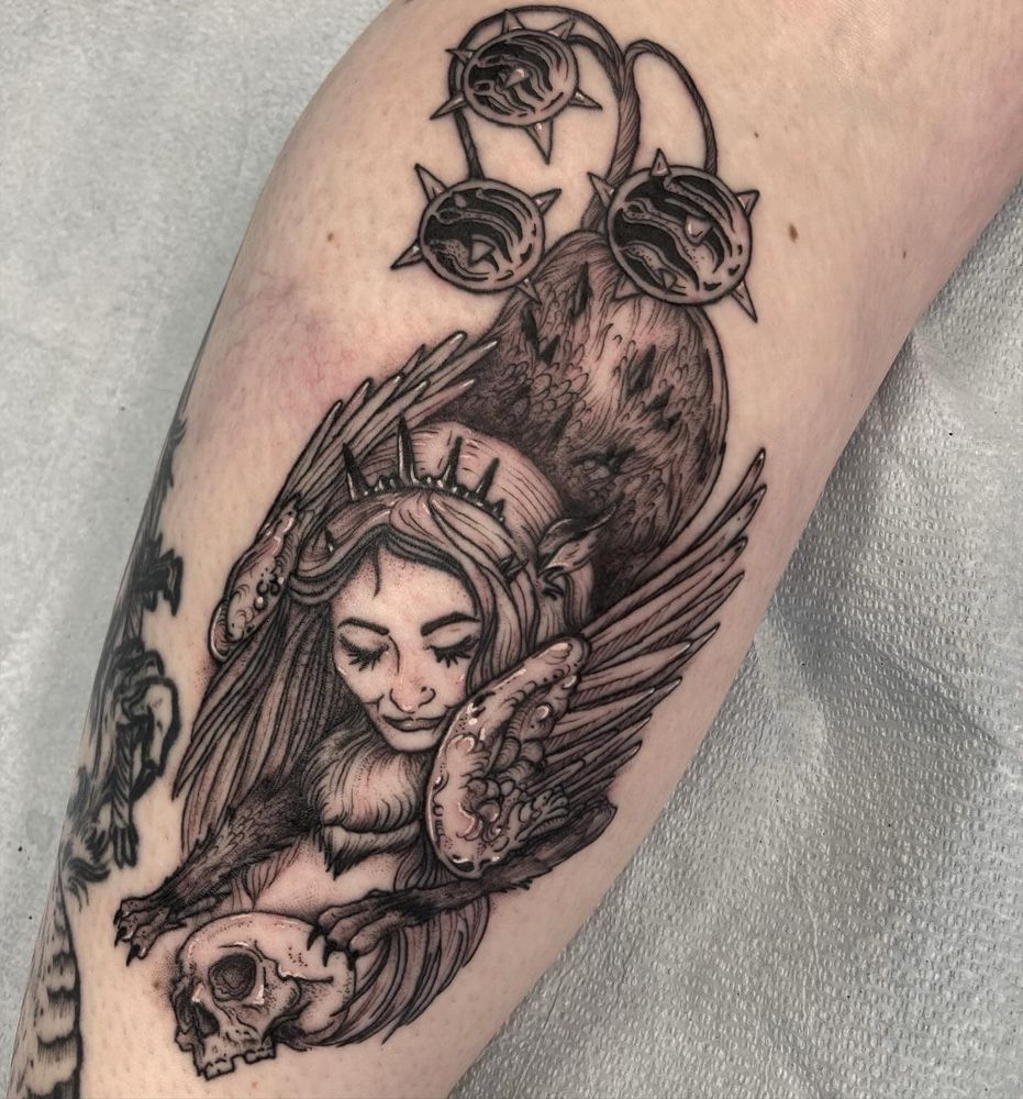 Tattoo on a leg of a creature with a human head, winged griffin body, and three spiky flail balls as a tail. The creature is playing with a human skull. 