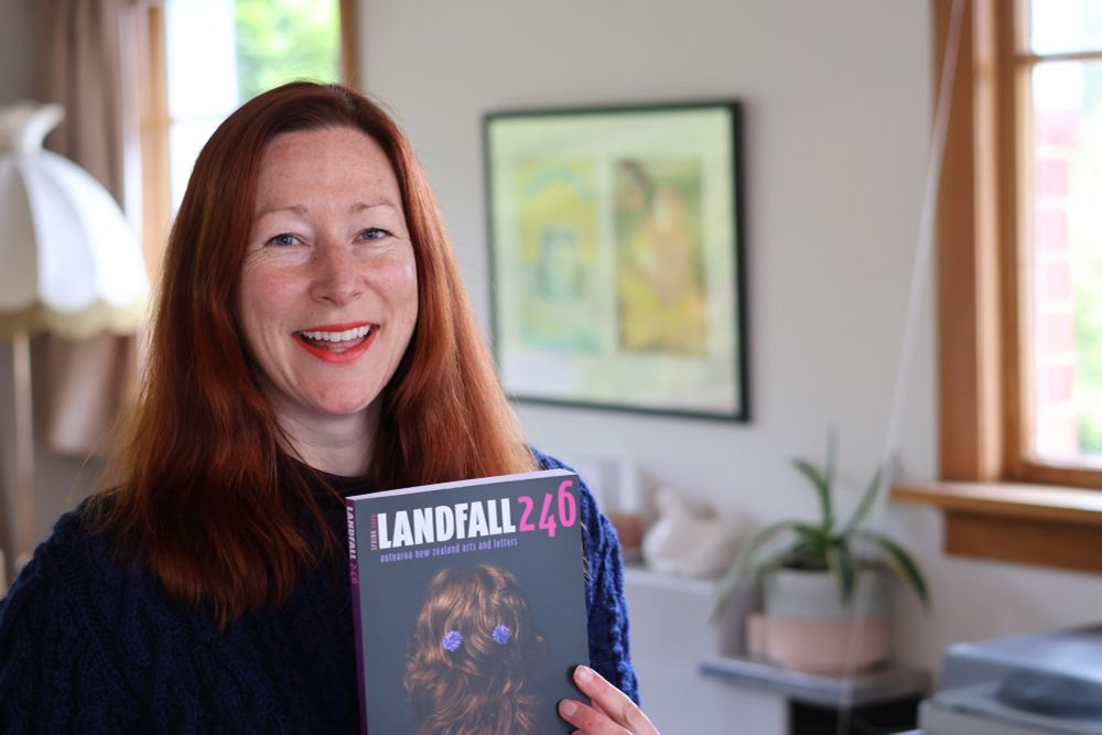 Woman posing with a copy of the Landfall Journal
