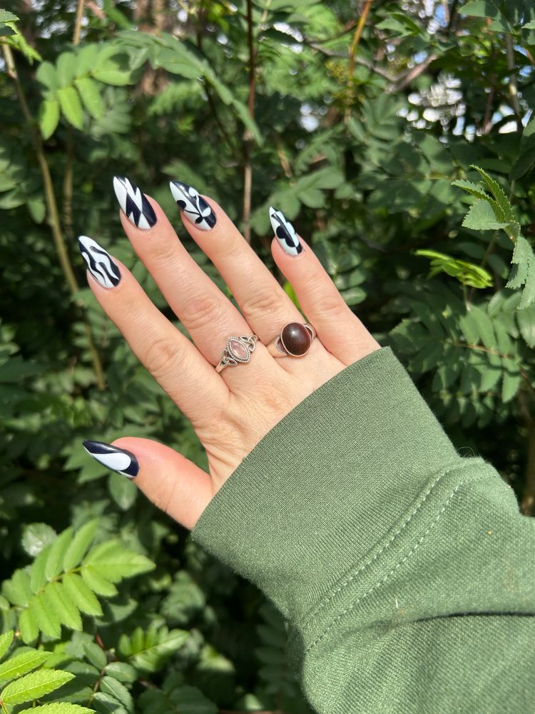 Picture of a hand in front of greenery, showing off a black and white coloured manicure