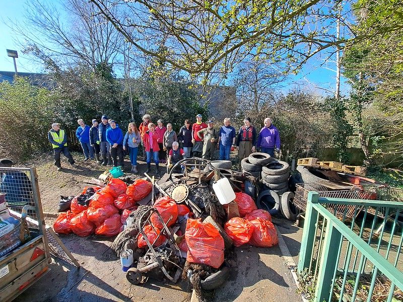 Group of litter pickers standing behind a pile of litter including red bags , car tyres and metal.