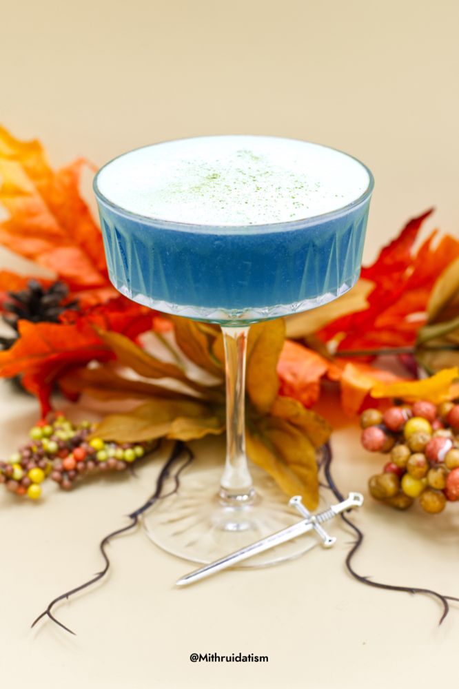 A blue non alcoholic drink in a coupe glass decorated against an autumn themed background 