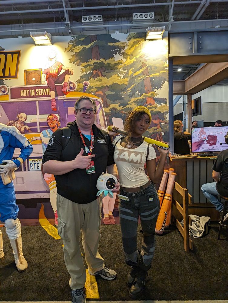 An old man pointing at a cosplay of a video game character, smiling.