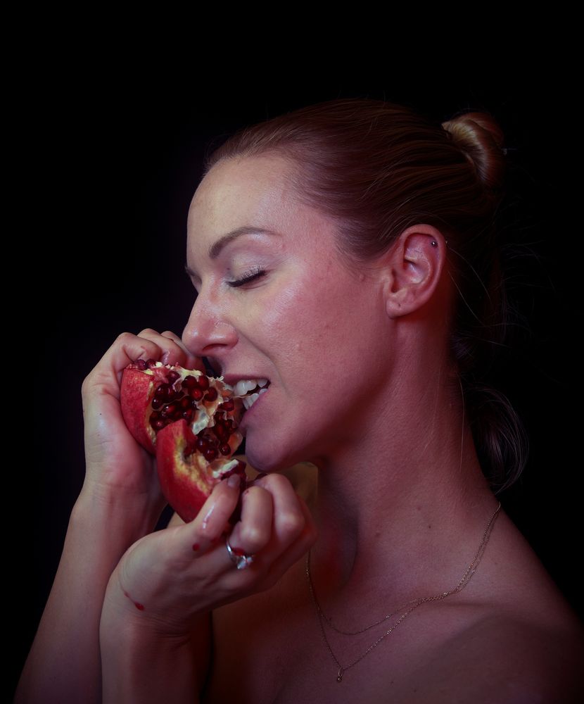 Marie biting into a pomegranate cut open.