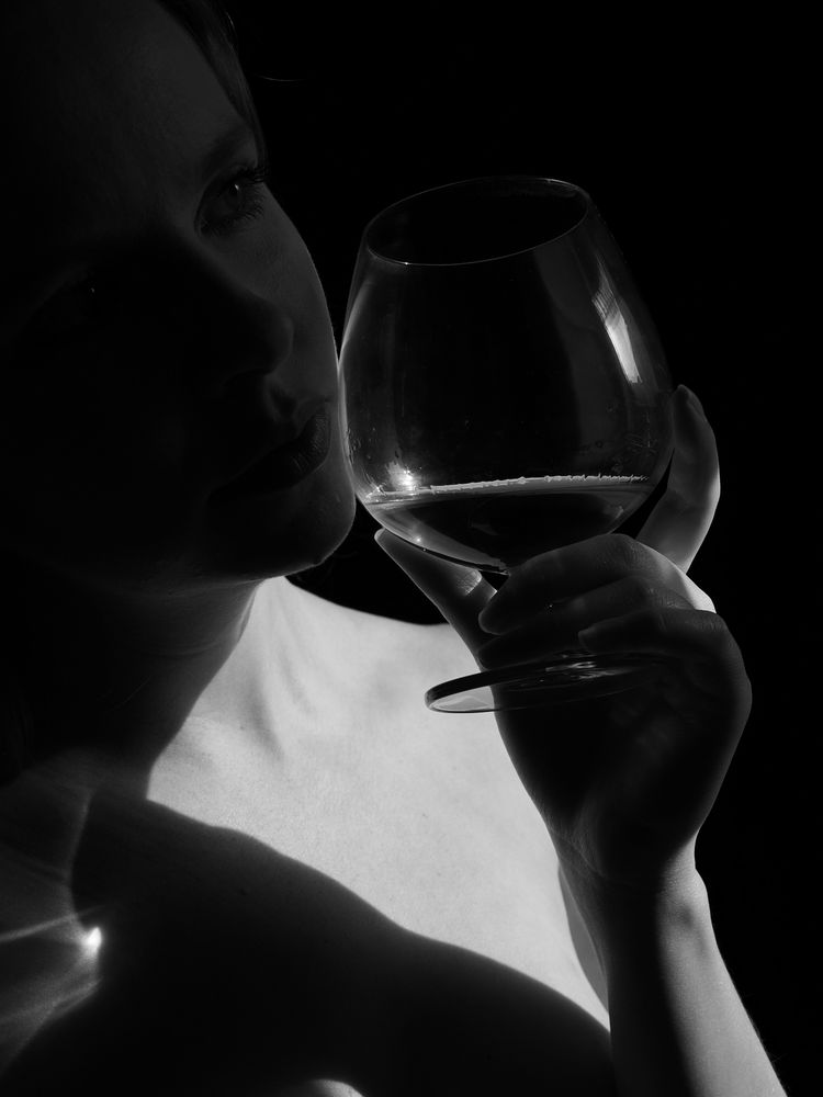 Charlotte holding a snifter by the window. A concentration of light on the glass is refracted on her skin.