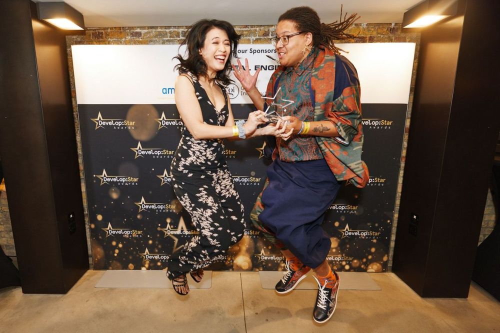 Anisa and Jonas are jumping mid-air both looking very excited while holding the Develop Star award between them