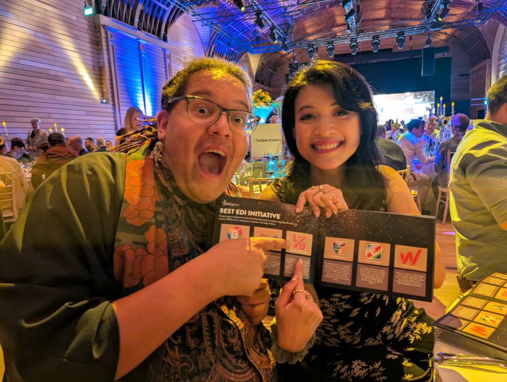 Jonas and Anisa are holding the programme for the awards, with the page open to the Best EDI Initiatives. They are pointing at the Limit Break logo
