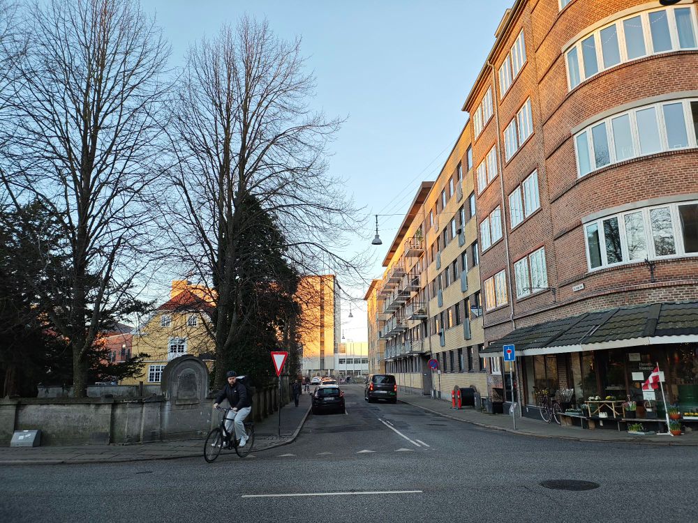 Photo of a cityscape from a road junction. The sunlight can be perceived at the top of the buildings.