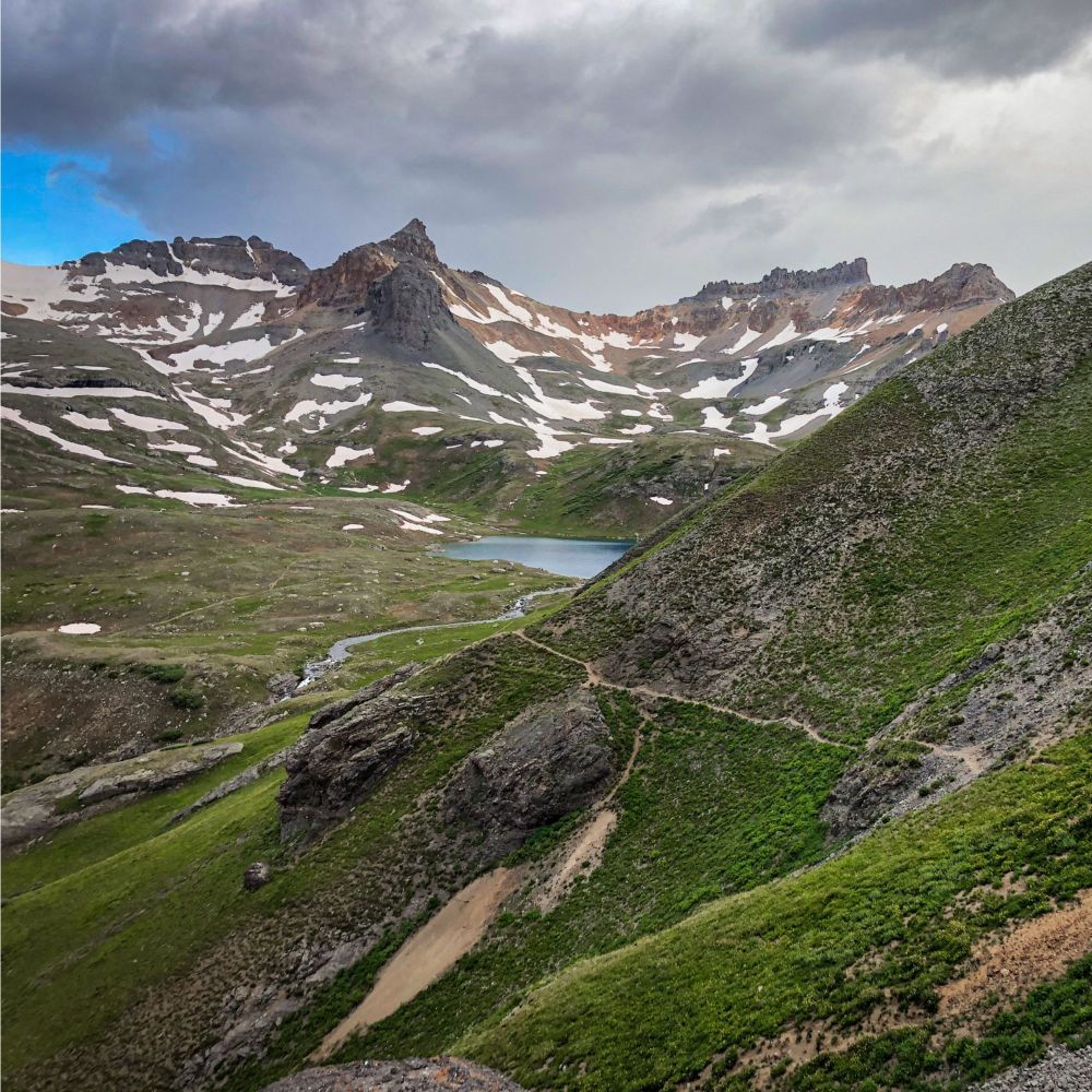Photo of alpine mountain tops ribboned with snow and a lake in the valley below.