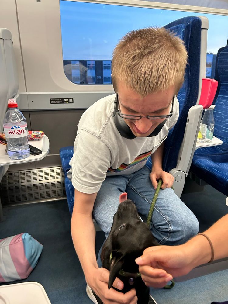 A photo of me and a black dog on a train. The dog has its tongue out and I am looking at it affectionately. 