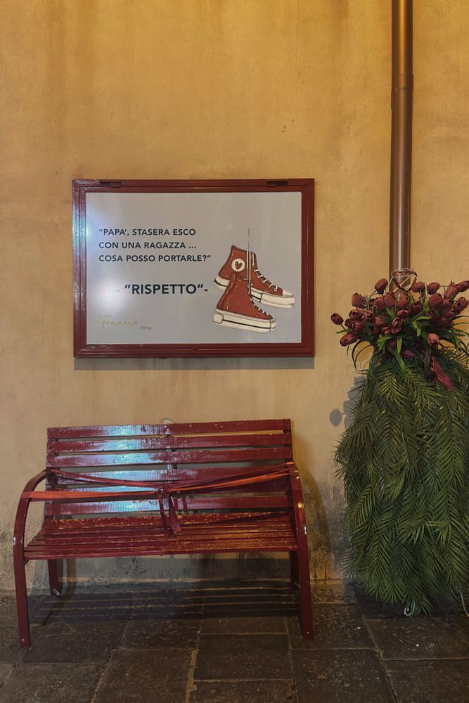 Rood bankje met een rood lint met daarboven de tekst in het Italiaans. 