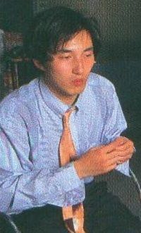 another picture of young suda, in the same location and in the same outfit. you can see that he’s also wearing black trousers. he also looks like he’s talking here, this time looking downwards and with his hands together 