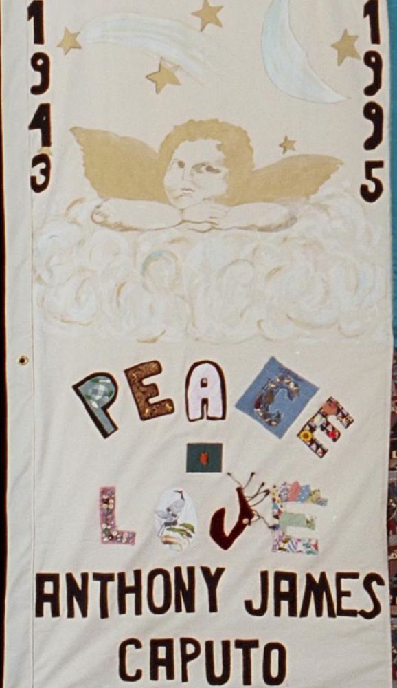 Commemorative square in the AIDS Memorial Quilt honoring Anthony James Caputo. The "square" is a cream rectangle, portrait orientation, with his birth and death years (1943 and 1995) on either vertical margin framing the golden cherub head, with moon and stars above and clouds below. PEACE and LOVE are spelled with letters symbolizing his interests and talents, underneath the cherub. His three names below that sign-off are in the same dark blocks as his years. Thirty years gone, and of course I still remember his favorite angel motif. A darling man, much mourned even now.