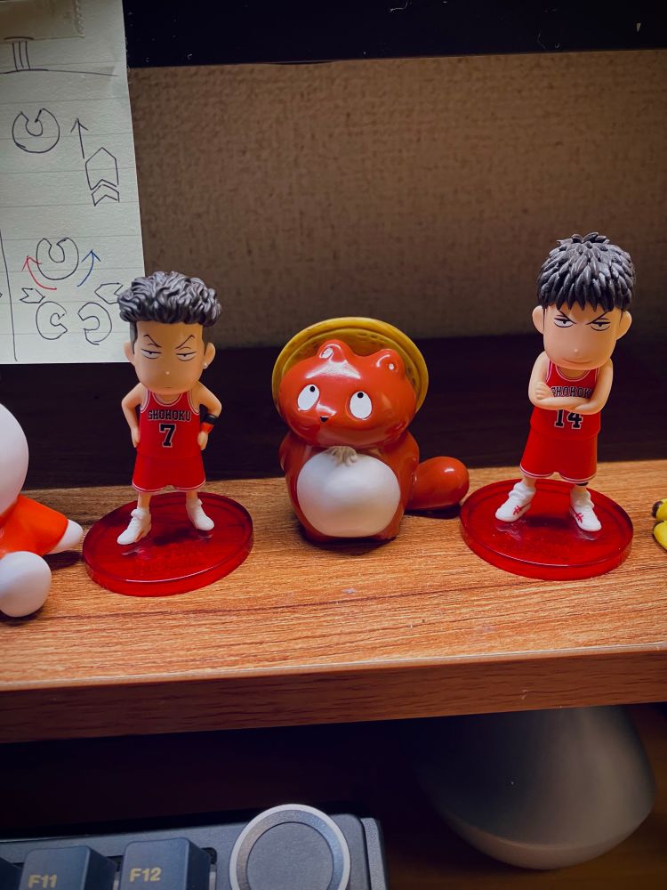 モニタースタンドに置かれたリョータと三井のデフォルメフィギュアの間に茶色のぼんやり子たぬきのソフビを置いている写真。