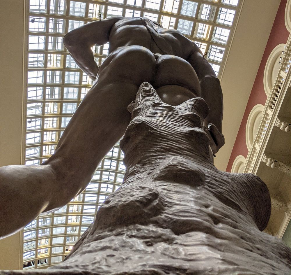 A photo looking up, at the back of the Michelangelo's David cast, showing his prominent bum and muscled back in high relief