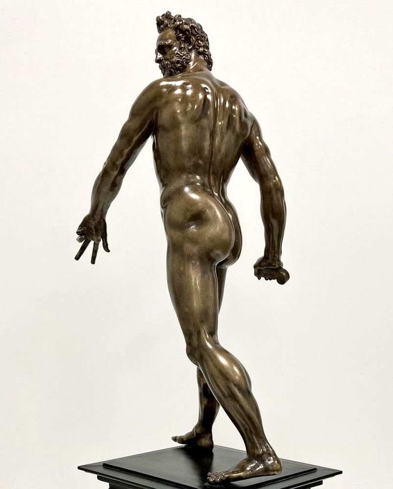 A bronze statue which has been polished to a high shine, of a striding figure, photographed from behind so it looks like they're walking away from the viewer