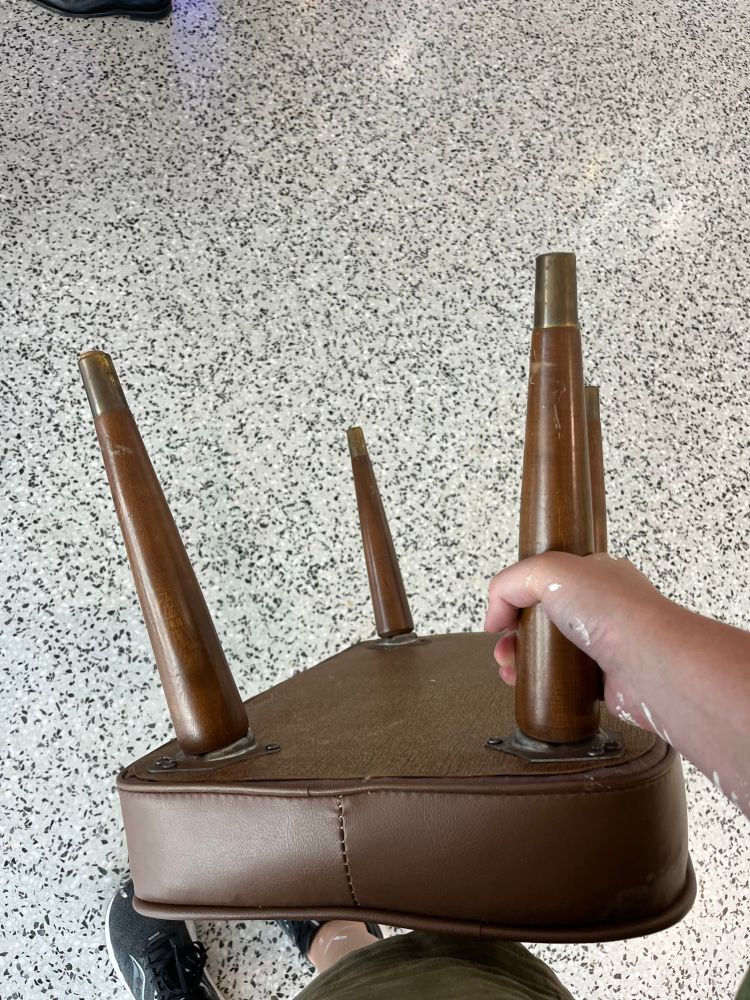 A picture of a brown vintage footstool being held by one leg as I stand in line for train boarding