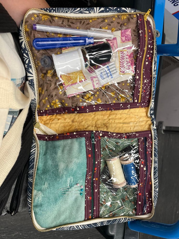 The quilted pouch open to reveal a variety of sewing notions in various vinyl and cotton pockets 