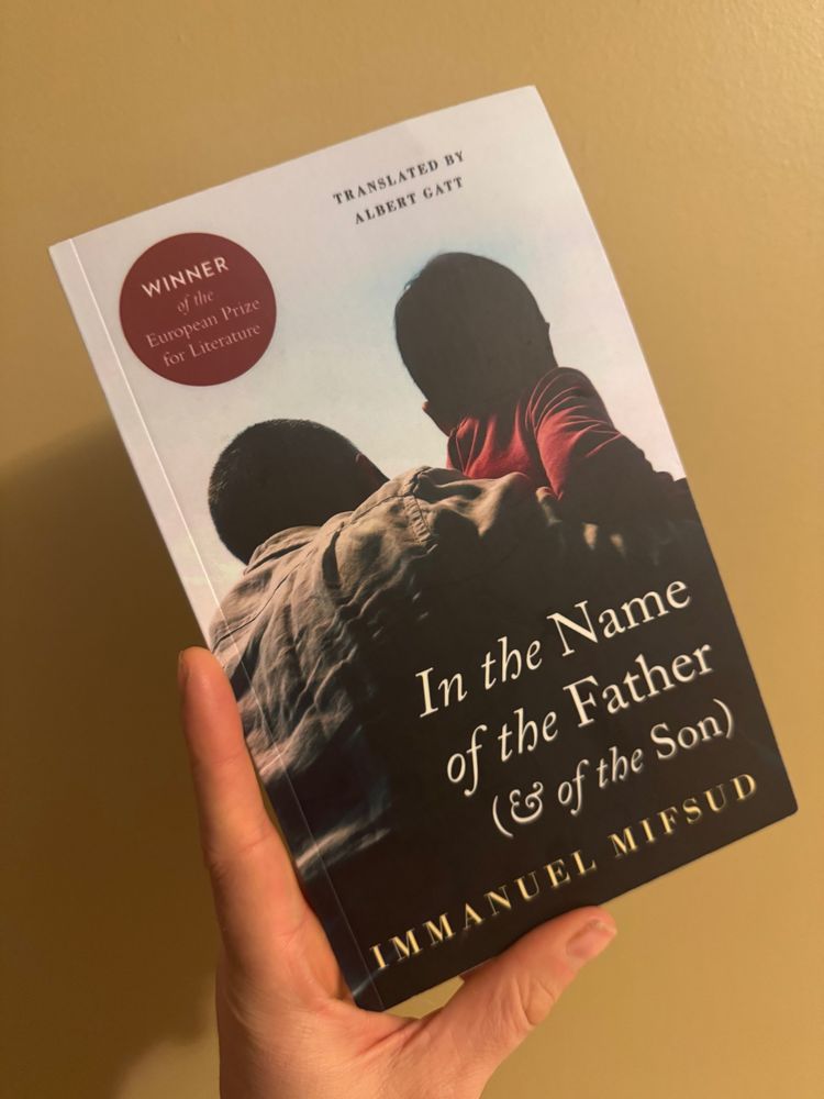 Me holding the book up in one hand. The image shows a father, holding his young son in his arms. We can only see their backs 