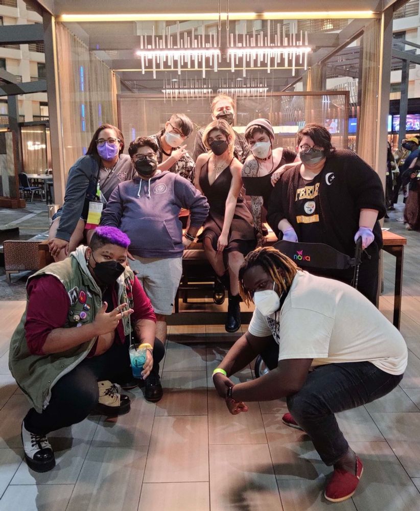 A photo of the Transplanar Cast sitting and stacking around a lobby together. Everyone is masked and posing together under a fancy light. The photo features: Dare, Val, Samm, Connie, Cai, Hamnah, Sea, quinn, and Austin.