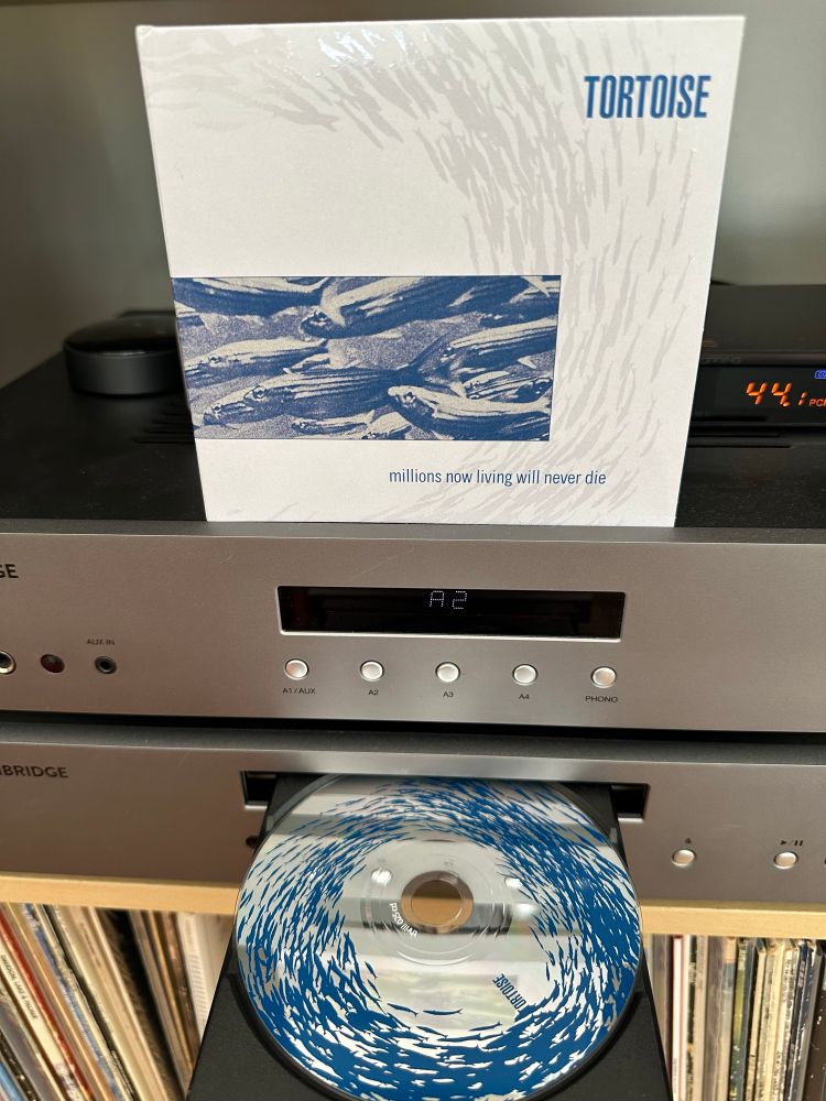 The picture shows a cd of the Tortoise album Millions Now Living Will Never Die waiting expectantly in the cd tray. The CD is also pictured.