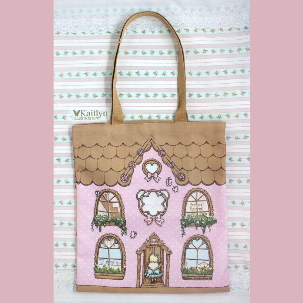 A Goldilocks themed tote bag with a pink house on the front with brown shingles and a brown strap. There are 4 windows and Goldilocks is about to open the door.