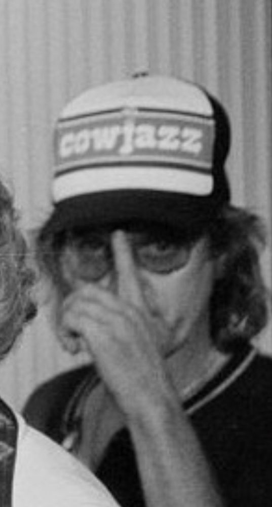 Man with ‘COWJAZZ’ hat and finger in front of face. 