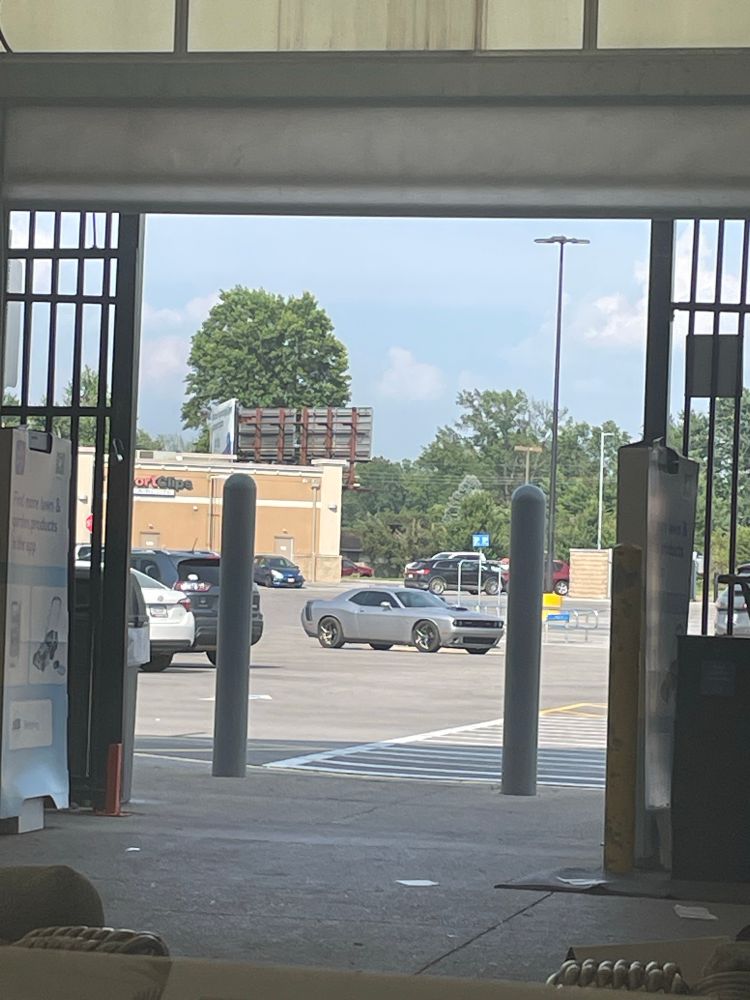 An image taken from the garden section of a store, an open iron gate leading out to a parking lot and other stores.