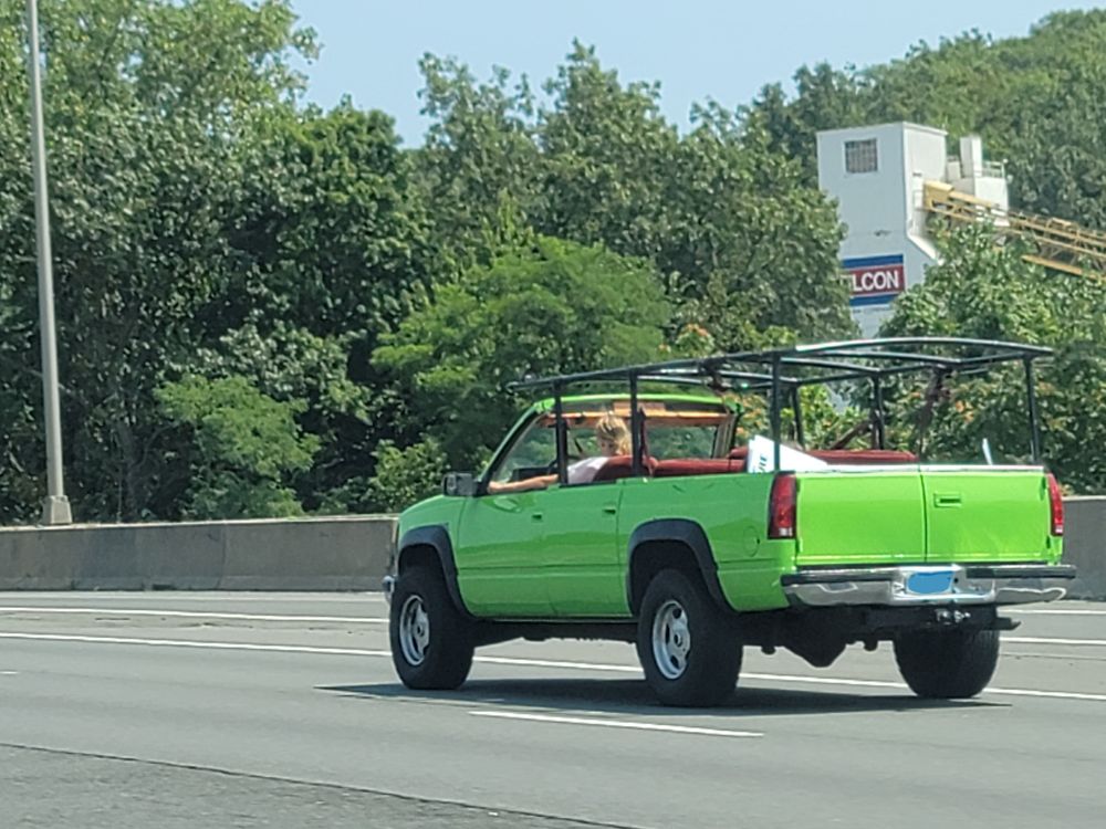 An old Chevy Suburban, painted bright green, with the roof chopped off and a weird metal frame put in its place