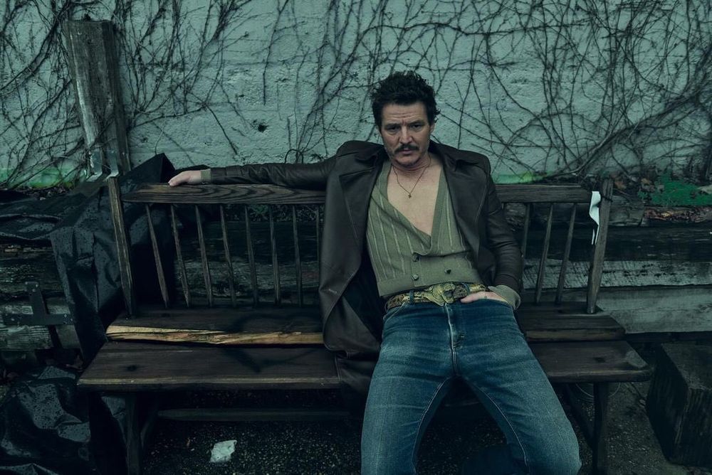 Pedro Pascal photoshoot for Esquire Magazine 2023 featuring him wearing a cardigan vest under a blazer stretched out on a park bench