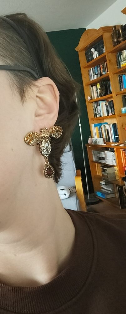 Photo of me wearing the pretty big moth earrings. They are golden with a lot of rhinestones and the wings are spread out so it's touching my cheeks
