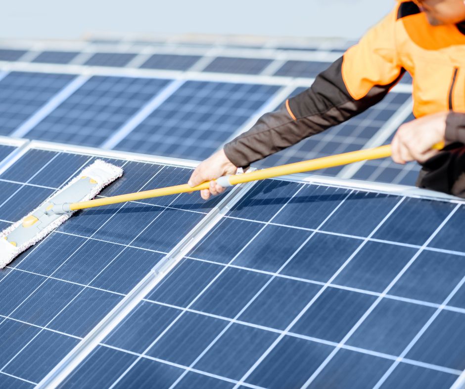 A professional cleaner in protective workwear diligently cleaning solar panels with a mop. This image represents a solar power farm cleaning service, emphasising the importance of maintenance in renewable energy solutions.