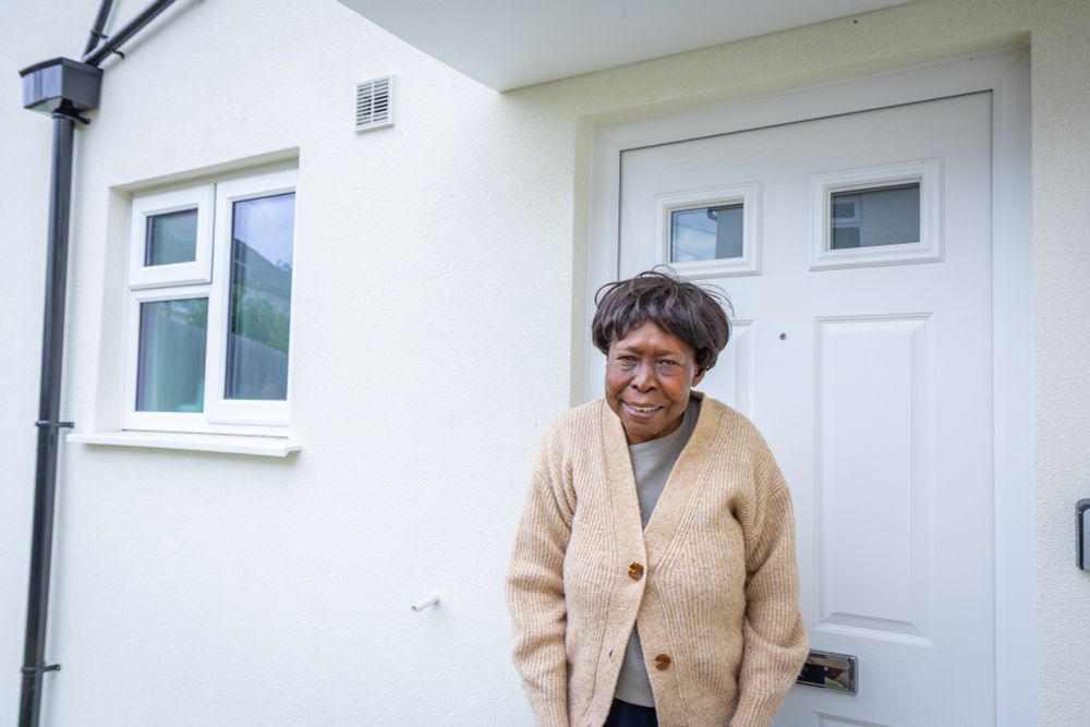A resident proudly stands in front of their newly retrofitted home, highlighting the improved window and door replacements that enhance energy efficiency and aesthetics.