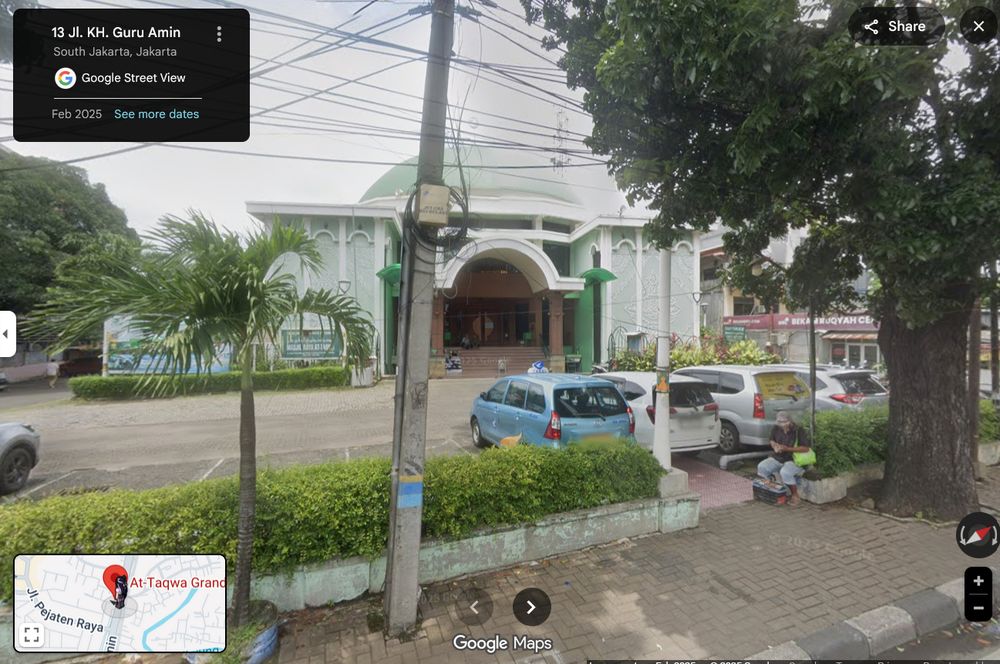 screenshot from google maps showing a street scene in Indonesia, with trees and hedges in the foreground, a city street in the middle ground and a domed mosque building on the other side of the street. some vehicles are parked on this side of the street.